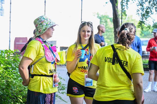 Drei Volunteers der Hamburg 7s stehen in gelben T-Shirts mit Volunteerschriftzug auf dem Rücken im Kreis zusammen