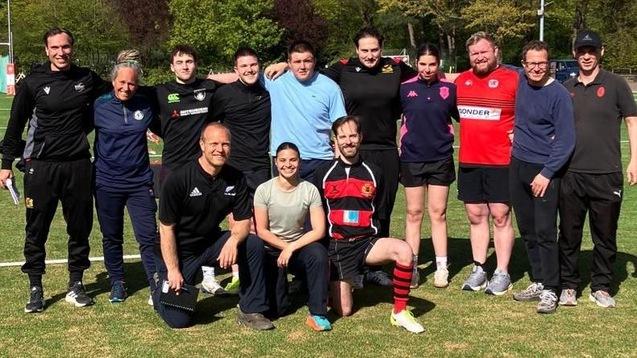 Eine Gruppe von 13 männlichen und weiblichen Trainern und Trainerinnen bei Sonneschein auf dem Kunstrasenplatz der Rugby-Arena Stadtpark